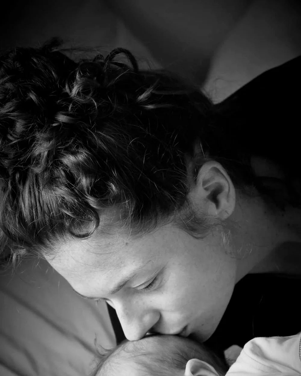 Photographie en noir et blanc d'une mère embrassant la tête de son nouveau-né