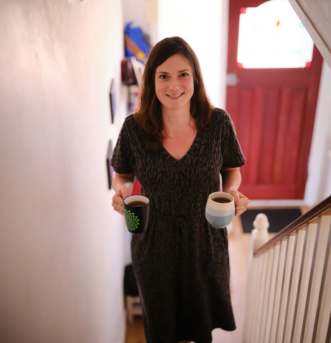 Elodie smiling as she carries two mugs of tea up the stairs
