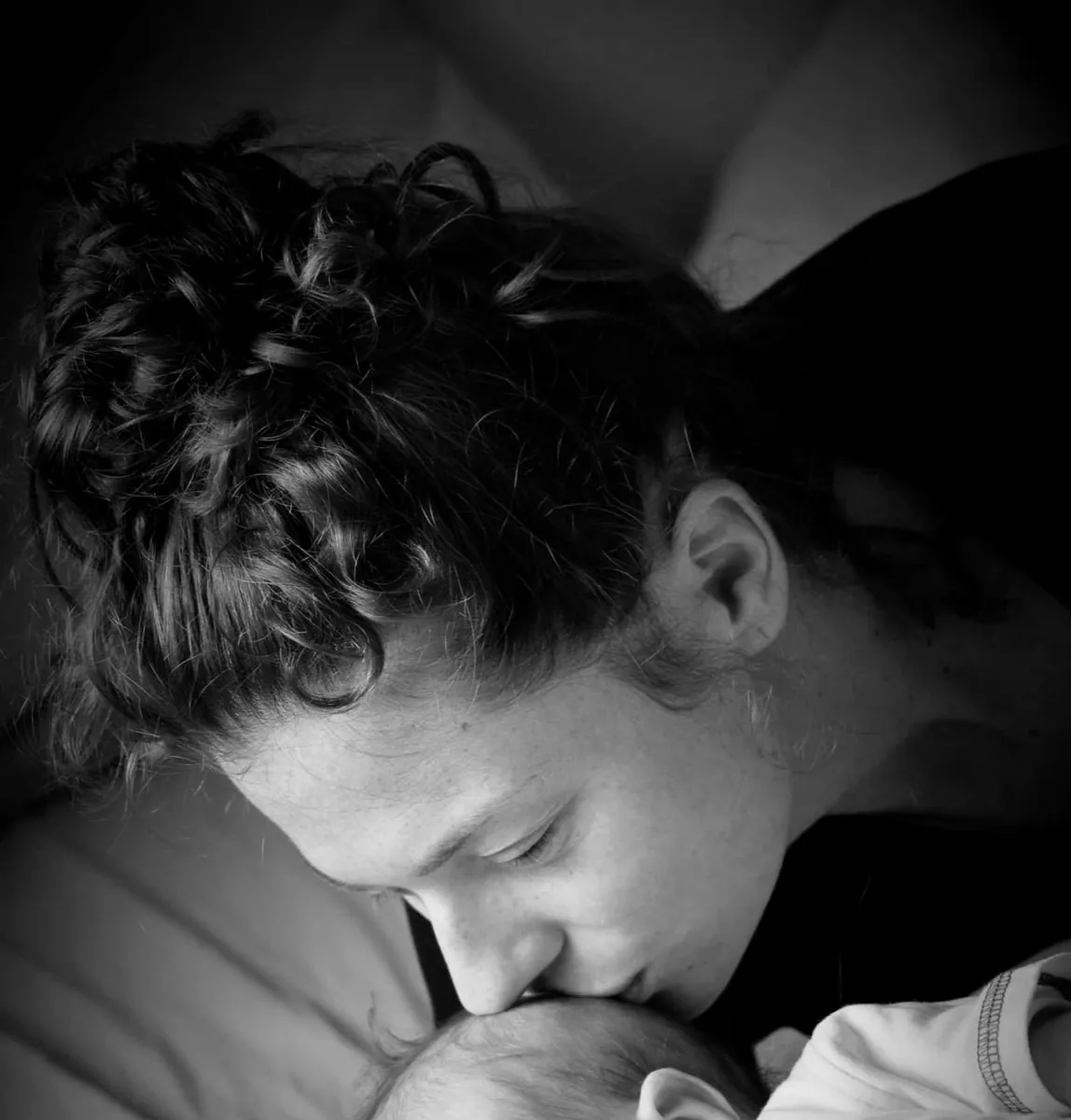 Black and white photograph of a mother kissing her newborn's head