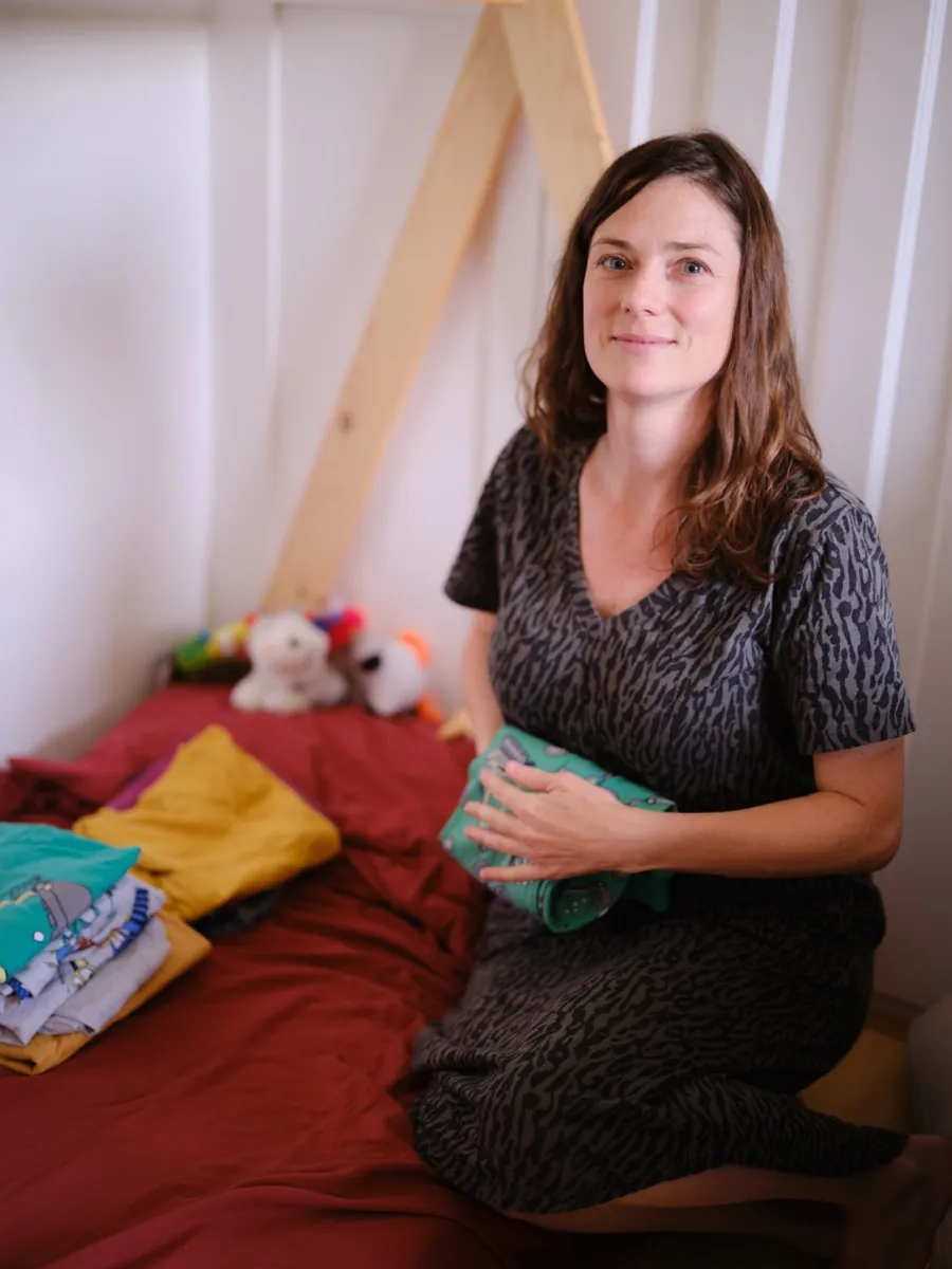 Elodie sitting on a child's bed with folded baby clothes